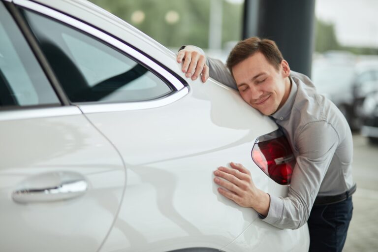 Muž sa opiera o nové biele auto v autosalóne