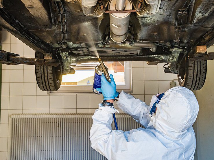 Technik v ochrannom obleku nanáša antikoróznu ochranu na podvozok auta